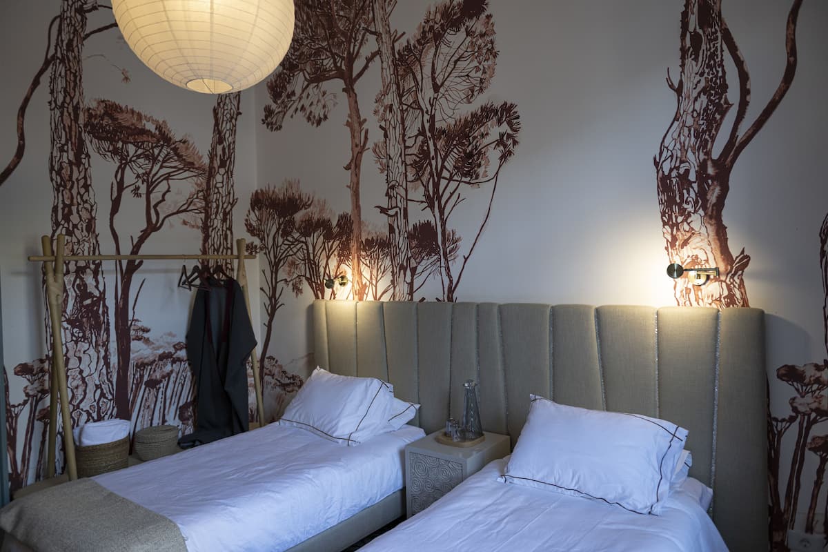 A hotel room with two beds, a large wall mural, and a hanging light fixture.