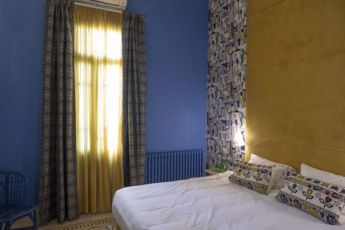 A bedroom with a bed, curtains, a radiator, and a patterned wall.