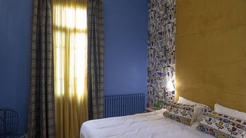 Un dormitorio con cama, cortinas, un radiador y un papel tapiz estampado.