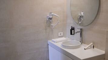 A bathroom with a white sink, a round mirror, a handheld showerhead, and a toilet.