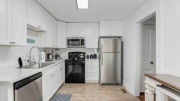 A modern kitchen with white cabinets, a stainless steel refrigerator, a microwave, an oven, and a dishwasher.