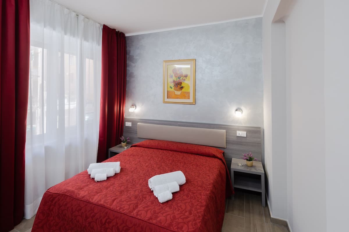A hotel room with a bed, a nightstand, a wall-mounted light, and a painting.