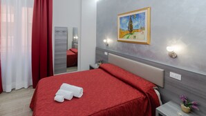 A hotel room with a large bed, a painting on the wall, and a nightstand with a lamp. - AFFITTACAMERE ALESSIA (Sanremo)