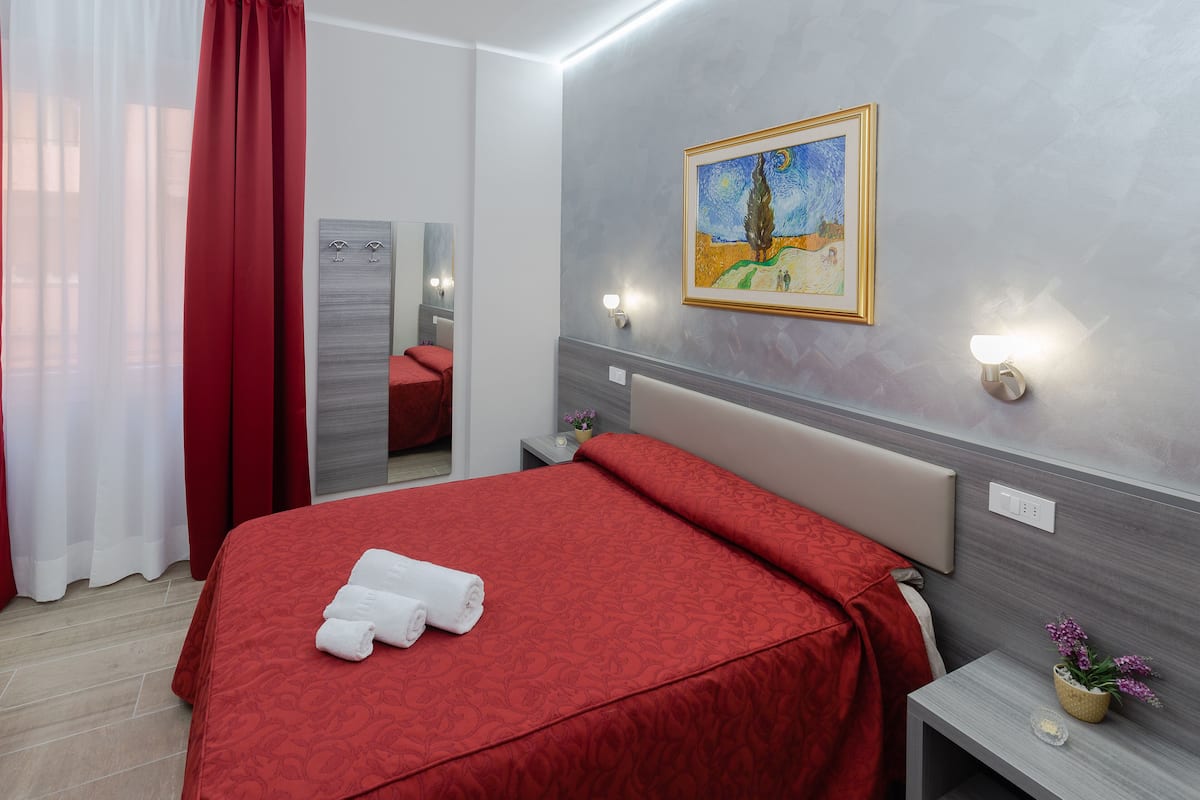 A hotel room with a large bed, a painting on the wall, and a nightstand with a lamp.