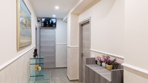 A hallway with a glass display case, a wooden door, and a reception desk with flowers. - AFFITTACAMERE ALESSIA (Sanremo)