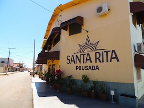Um edifício com uma placa indicando 'Santa Rita Pousada' e uma fileira de vasos de plantas ao longo da calçada.