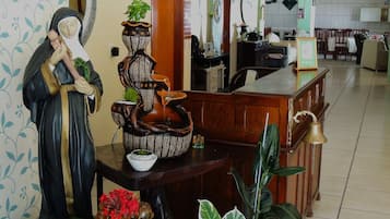 A room with a wooden reception desk, a statue, a decorative vase, and a bell.