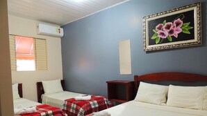 A hotel room with two beds, a red and blue checkered blanket on one bed, a painting of flowers on the wall, and an air conditioning unit.