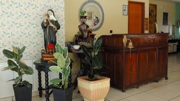 Um quarto com uma mesa de recepção de madeira, uma estátua, plantas em vasos e um espelho na parede.