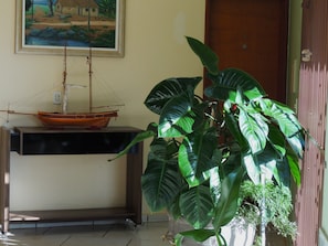 Una habitación con un modelo de barco en un estante, una planta verde grande y un cuadro en la pared.