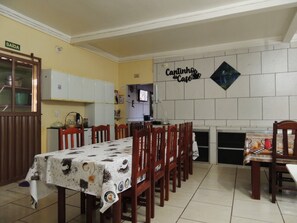 A dining area with a table set for six, wooden chairs, a kitchen area with cabinets, and a wall sign that reads 'Cantinho do Cafe'. - Pousada Santa Rita (Abadiania)