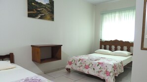 A bedroom with two beds, a wooden headboard, a small wooden shelf, and a painting on the wall.