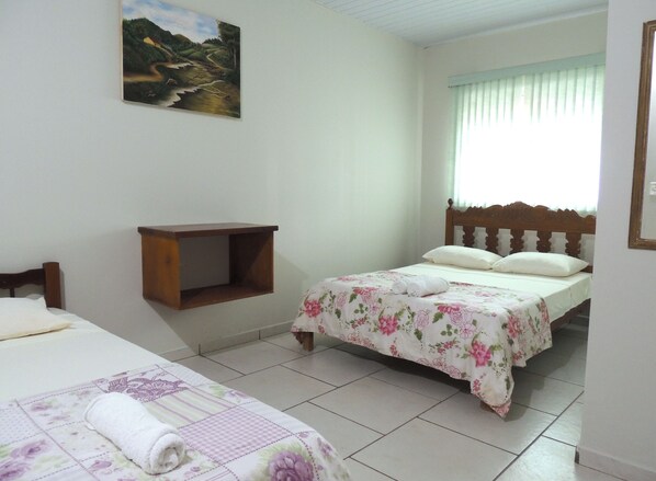 A bedroom with two beds, a wooden headboard, a small wooden shelf, and a painting on the wall. - Pousada Santa Rita (Abadiania)