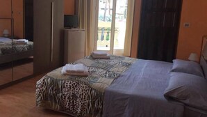 A bedroom with a bed, a wardrobe, a television on a stand, and a view of the outside. - LOCANDA BEATRICE (Sanremo)