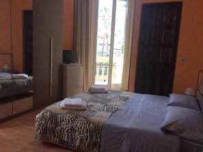 Ein Schlafzimmer mit Bett, Schrank, Fernseher auf einem Schrank und Blick ins Freie.
