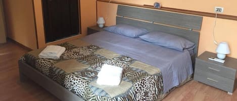 Un dormitorio con cama, mesitas de noche, un cuadro y una puerta.