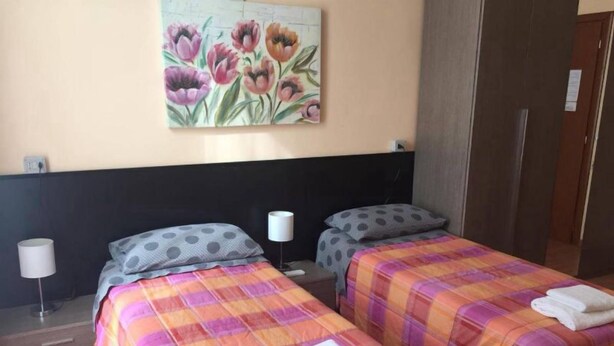 A hotel room with two beds, each with a plaid bedspread and pillows, a nightstand with a lamp, and a painting of flowers on the wall. - LOCANDA BEATRICE (Sanremo)