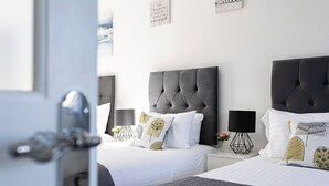 Une chambre d’hôtel avec deux lits, chacun doté d’une tête de lit capitonnée et de linge de lit blanc. On y trouve des tables de chevet avec des lampes et des coussins décoratifs.