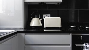 Une cuisine moderne avec des meubles blancs, un plan de travail noir, une bouilloire et un grille-pain.