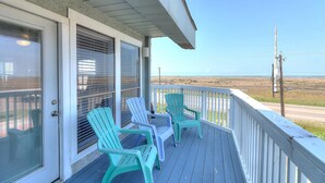 Un terrazzo in legno con due poltrone Adirondack, un portico coperto e vista sull'oceano.