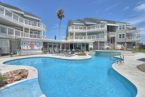 A pool area with a multi-level building, including balconies and a lifeguard stand. - This stylish condo is located on the second floor of Mustang Island Beach Club. (Port Aransas)