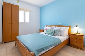 Ein Schlafzimmer mit Bett, Nachttisch, Lampe, Kleiderschrank und Fenster.
