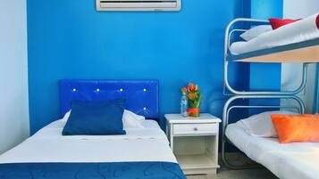 Habitación de hotel con literas, una cama individual, una mesita de noche con un florero y un aire acondicionado de pared.