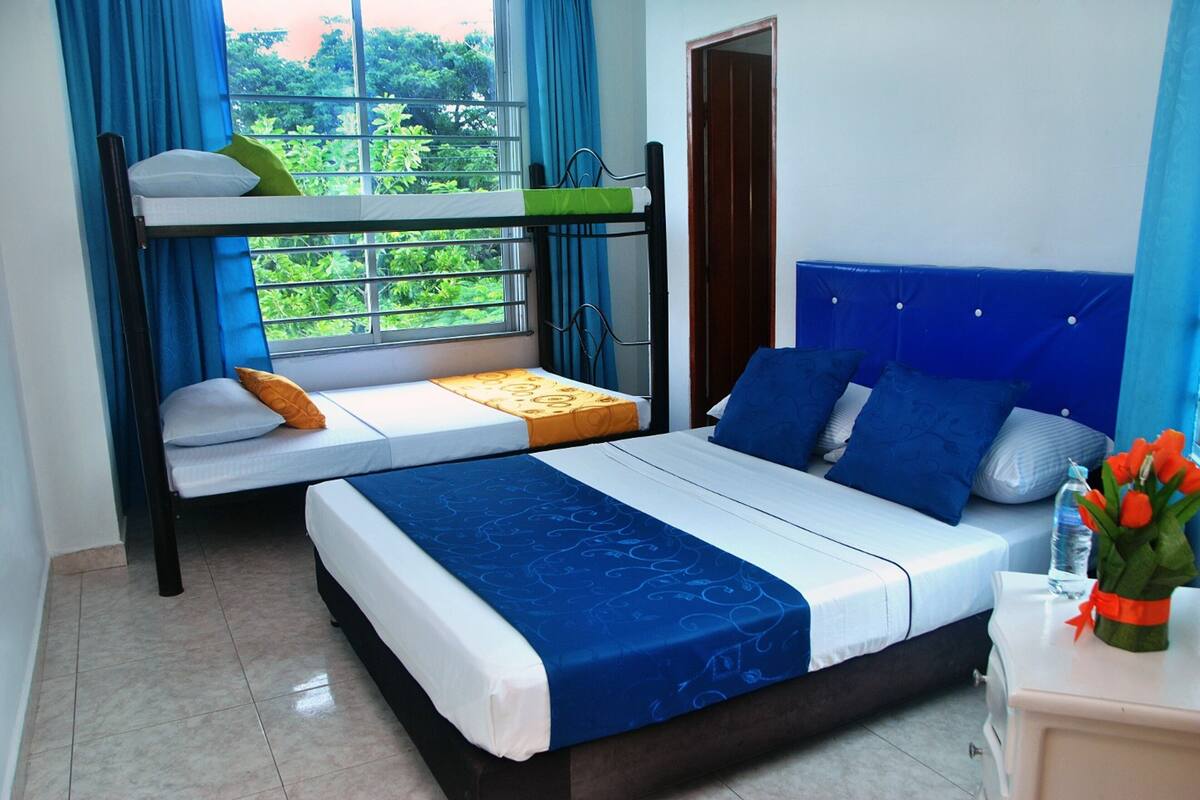 A bedroom with a bunk bed, a single bed, and a nightstand with a vase of flowers.