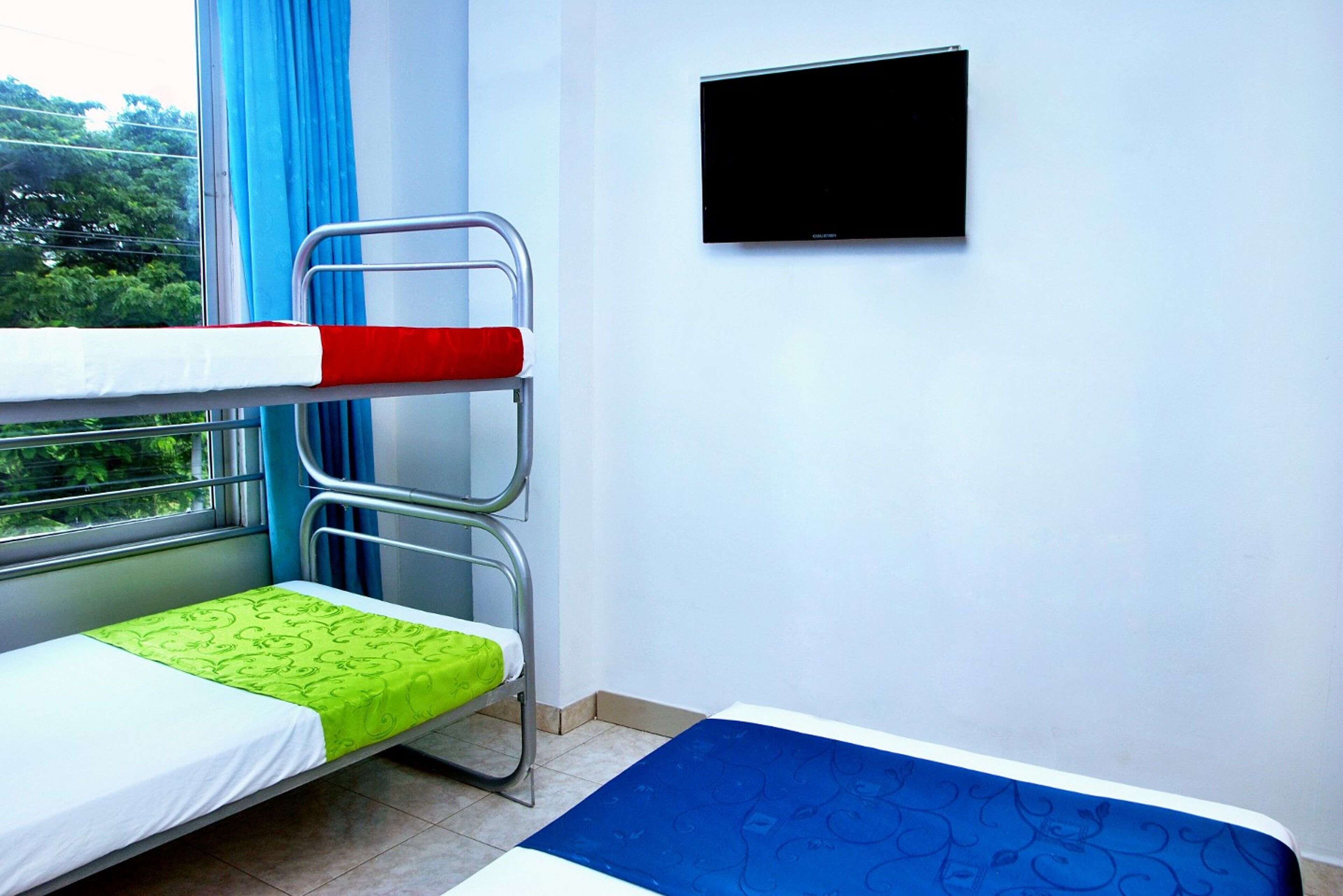 A room with bunk beds, a flat-screen TV, and a window with blue curtains.