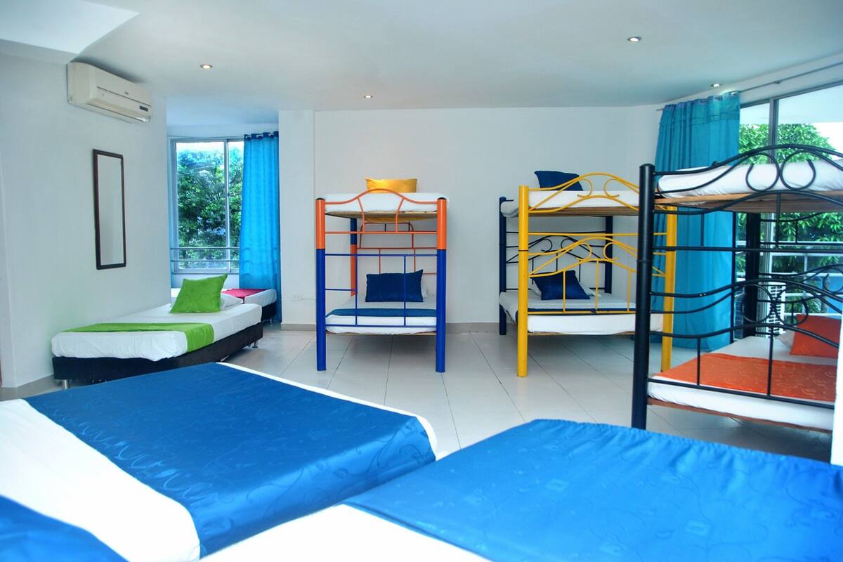 A hotel room with bunk beds, a sofa bed, and a large window offering a view of greenery.