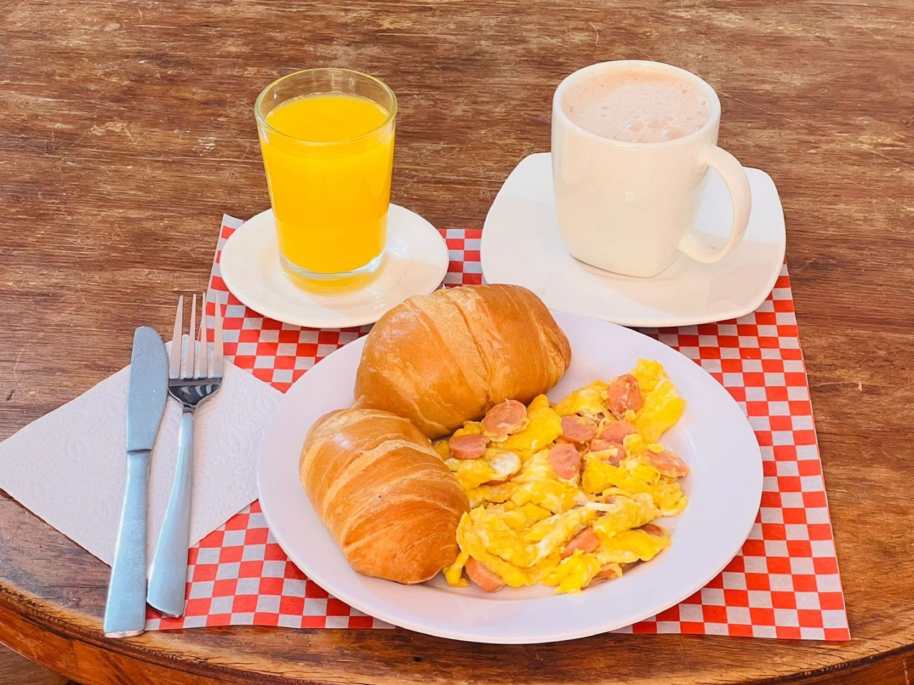 Un desayuno con croissants, huevos revueltos y una taza de café sobre un mantel a cuadros.