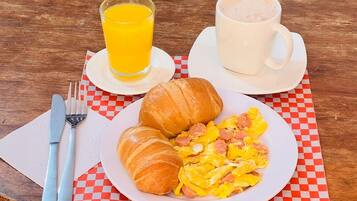 Un desayuno con croissants, huevos revueltos y una taza de café sobre un mantel a cuadros.