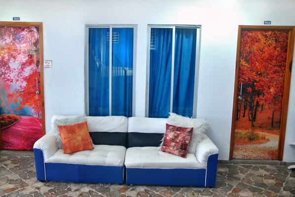 A two-seater sofa with blue and white cushions, positioned in front of a window with blue curtains.
