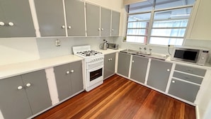 A kitchen with grey cabinets, a white countertop, a stove, a microwave, and a window with curtains.