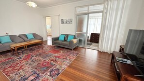 A living room with a sofa set, a coffee table, a patterned rug, a television, and a sliding glass door leading to a balcony.