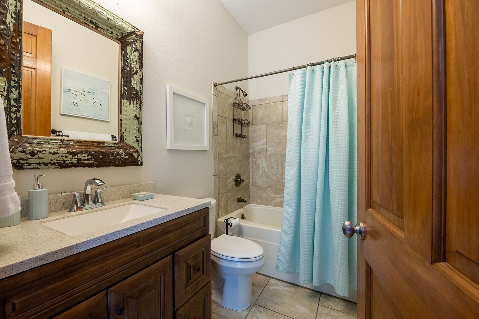 A bathroom with a wooden vanity, a white toilet, a bathtub, and a shower curtain.