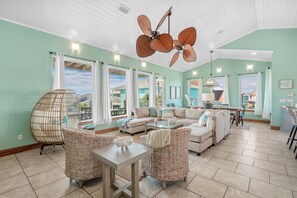 A spacious living room with a large ceiling fan, wicker furniture, and a view of the outside.
