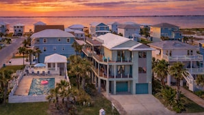 Un área residencial costera con varias casas de dos pisos, una piscina y vista al océano al atardecer.
