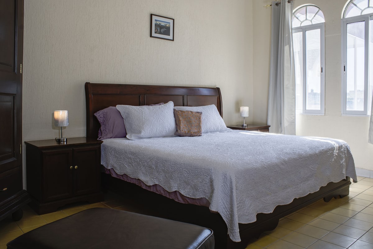 A neatly made bed with a white lace bedspread, a wooden headboard, and two bedside lamps.