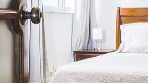 A bedroom with a wooden bed, a nightstand with a lamp, and a window with curtains. - Grand Domo Hotel (León)