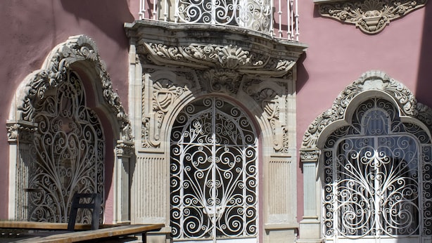 A pink building with ornate ironwork balconies and arched doorways. - Grand Domo Hotel (León)