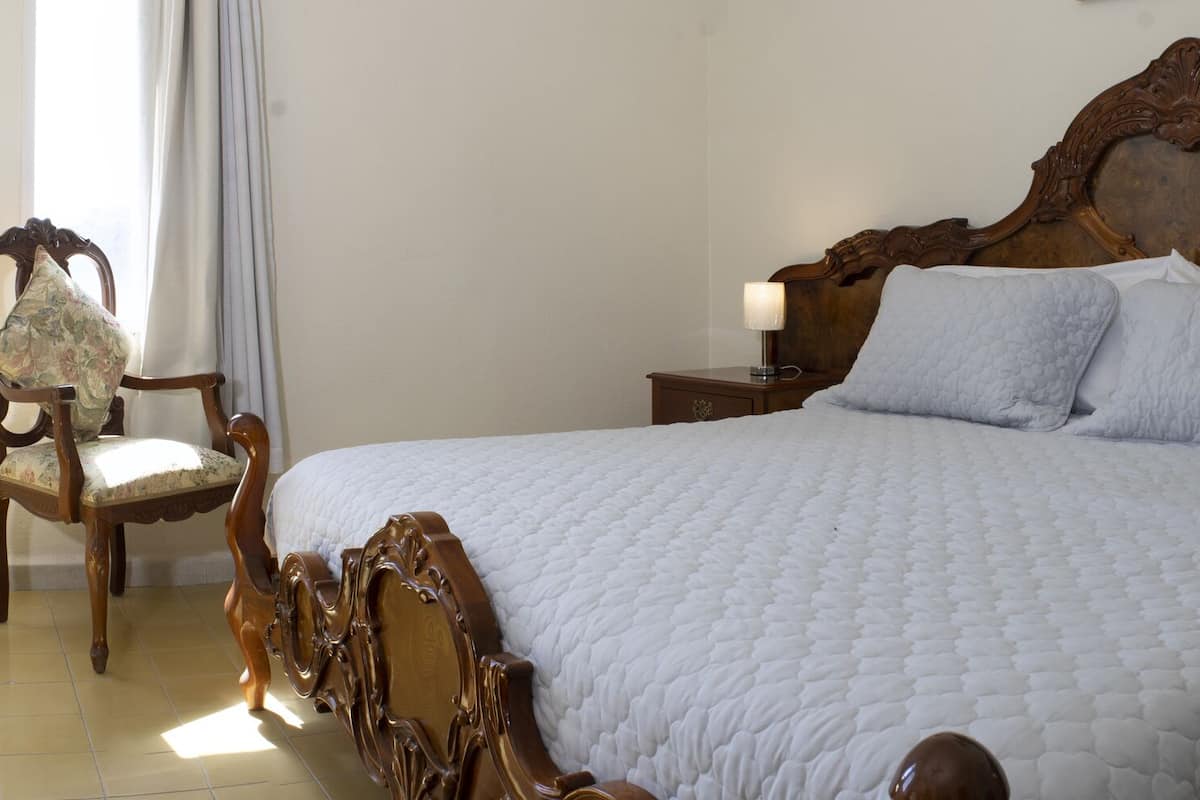 A bedroom with a wooden bed, a wooden dresser, a mirror, and a chair.