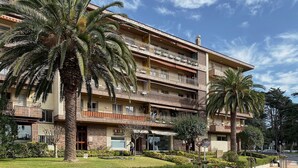 Un hotel de varios pisos con balcones, palmeras y un cielo despejado.