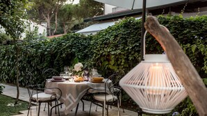 An outdoor dining area with a table set for four, surrounded by greenery and a white lantern.