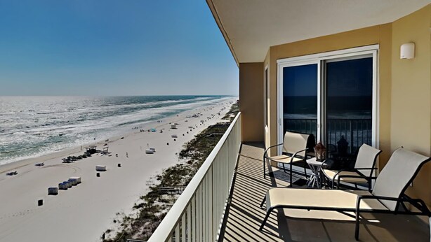 Een balkon met uitzicht op een strand, buitenmeubilair en een groot raam.