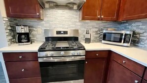 A kitchen with a stainless steel stove, oven, and microwave, wooden cabinets, and a tiled backsplash.