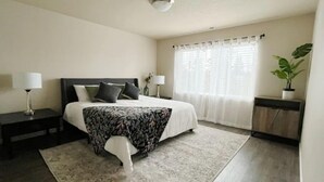 A neatly arranged bedroom with a bed, bedside tables, a potted plant, and a window with curtains.