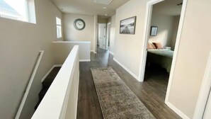 A hallway with a wooden floor, a white railing, a rug, and a clock on the wall.