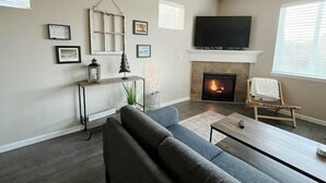 A living room with a fireplace, a sofa, a coffee table, and a TV mounted above the fireplace.