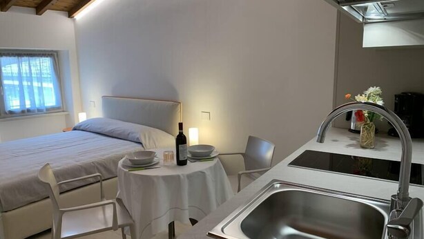 Een knus hotelkamer met een bed, een klein eettafeltje met borden en een fles, een wastafel en een stoel.